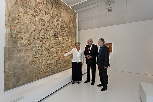 Drei Personen stehen vor einer großformatigen, altertümlichen Landkarte.