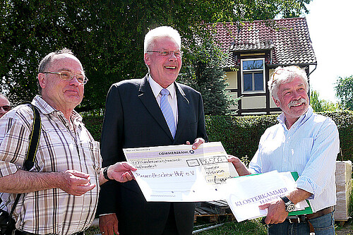 Drei Männer, darunter Klosterkammerpräsident Hans-Christian Biallas, halten einen übergroßen symbolischen Scheck.