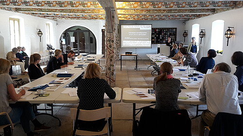 In einem mit Raum mit kunstvoll bemahlten Deckenbalken im Kloster Wienhausen sitzt eine Gruppe von rund 15 Personen zusammen.