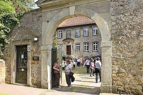 Eine Gruppe von Menschen bewegt sich durch ein steinernes Tor auf ein großes Gebäude zu.