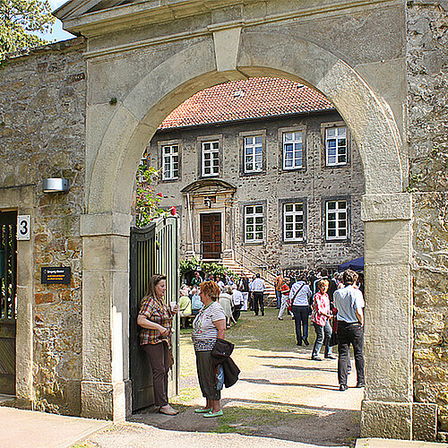 Eine Gruppe von Menschen bewegt sich durch ein steinernes Tor auf ein großes Gebäude zu.
