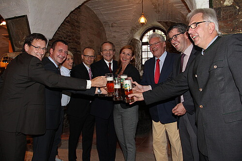 In einem Halbkreis stoßen Männer und Frauen mit jeweils einem Glas Bier an.