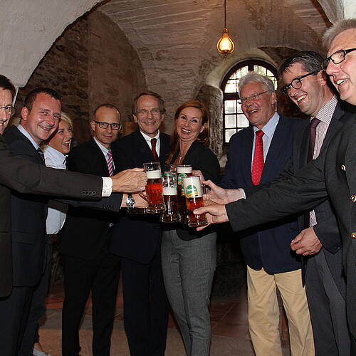 In einem Halbkreis stoßen Männer und Frauen mit jeweils einem Glas Bier an.