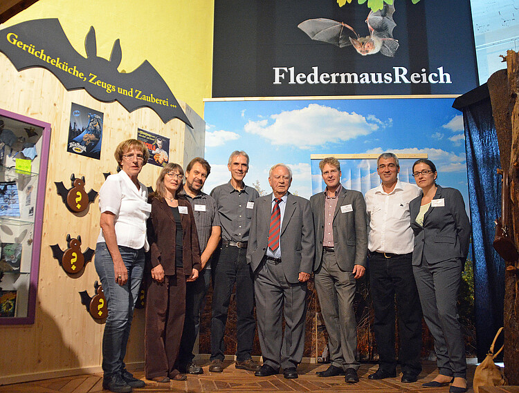 Eine Gruppe von drei Frauen und fünf Männern steht vor dem Eingang zu einer Fledermaus-Ausstellung.