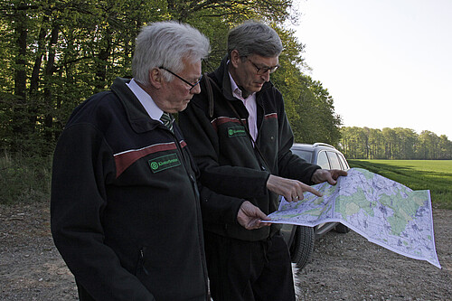Zwei Personen stehen am Waldrand und schauen gemeinsam auf eine Karte.