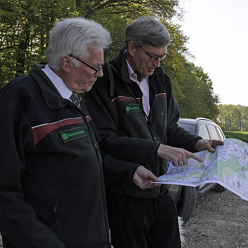 Zwei Personen stehen am Waldrand und schauen gemeinsam auf eine Karte.