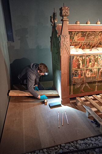Restaurator Johannes Mädebach kniet neben einen großen Kunstwerk aus Holz, um dieses aufbocken und so vor hereinlaufendem Wasser schützen zu können.